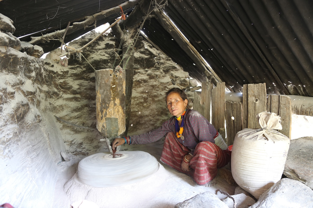 पानी घट्टमा अन्न पिस्दै मुगुकी महिला